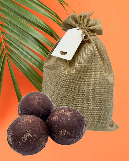 Three dark brown chocolate coconuts in front of a burlap bag with a tag on it, and orange background.
