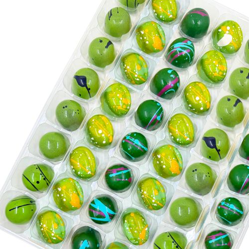 Assorted green chocolate bonbons in a clear plastic container on a white background