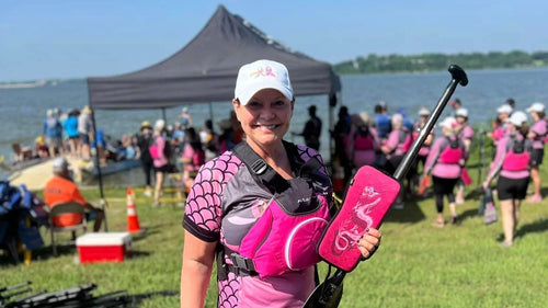 Woman in pink and black outfit with a backpack on a grassy area near a lake.