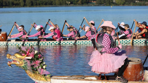 People in pink uniforms rowing dragon boats on a lake