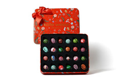 Set of colorful chocolates in a decorative box with a red lid featuring Christmas patterns and a bow, branded 'kate weiser'.
