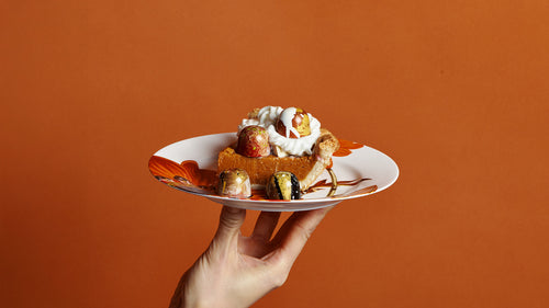 Hand holding a plate with a dessert against an orange background
